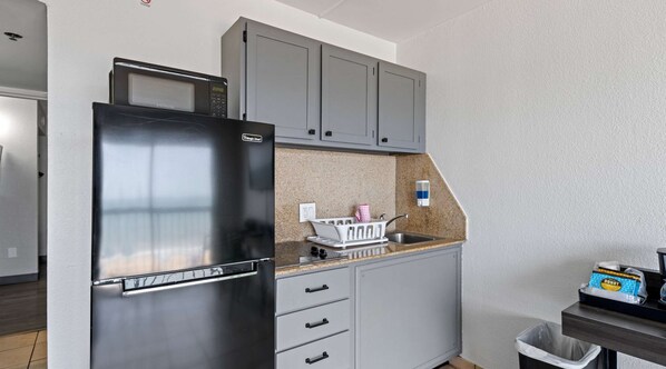 A compact kitchen with a stainless steel refrigerator, grey cabinets, a microwave, and a granite countertop. - SureStay Studio by Best Western Virginia Beach Oceanfront (Virginia Beach)