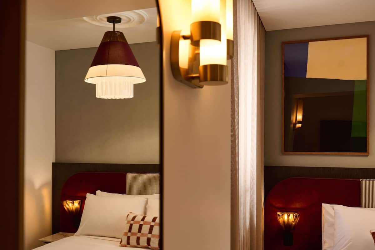 A hotel room with a bed, a mirror, and a pendant light.