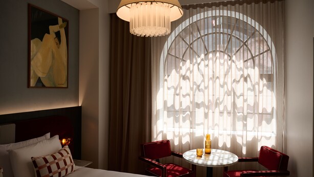 A hotel room with a bed, a round table with chairs, a chandelier, and a large window with curtains. - Hotel Morris Sydney - Handwritten Collection (Haymarket)