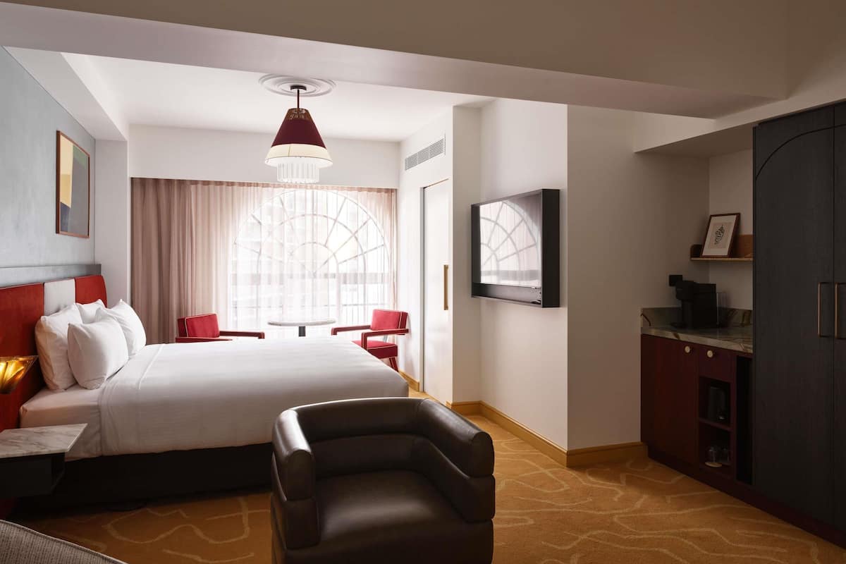 A hotel room with a bed, a desk, a chair, a TV, and a wardrobe.
