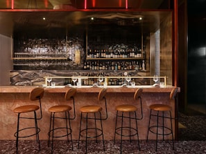 A bar area with a marble countertop, multiple stools, and a variety of bottles and glasses. - Hotel Morris Sydney - Handwritten Collection (Haymarket)