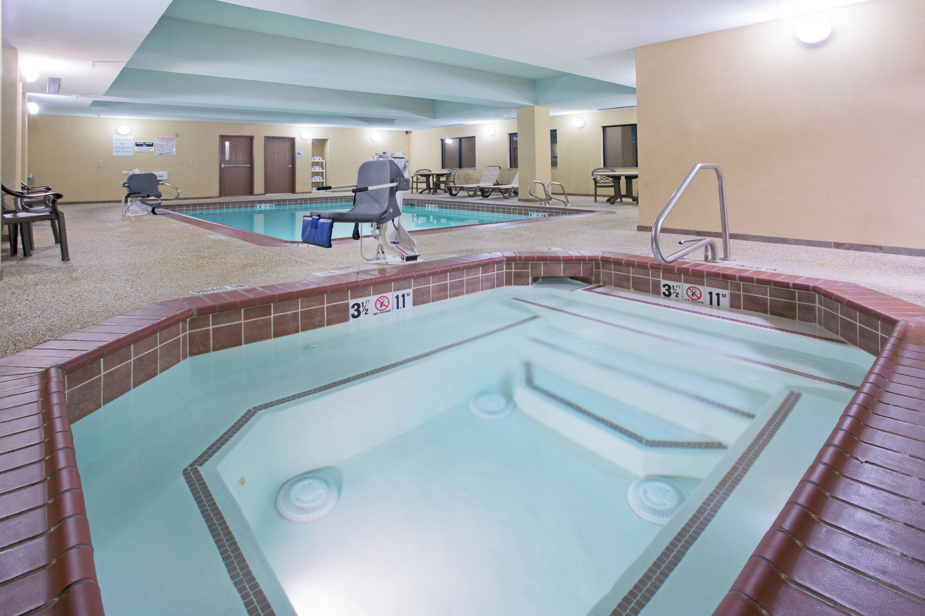 A hotel swimming pool area with two pools, lounge chairs, and a lifeguard chair.