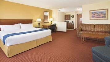 Quarto de hotel com uma cama grande, escrivaninha, sofá e cozinha compacta.