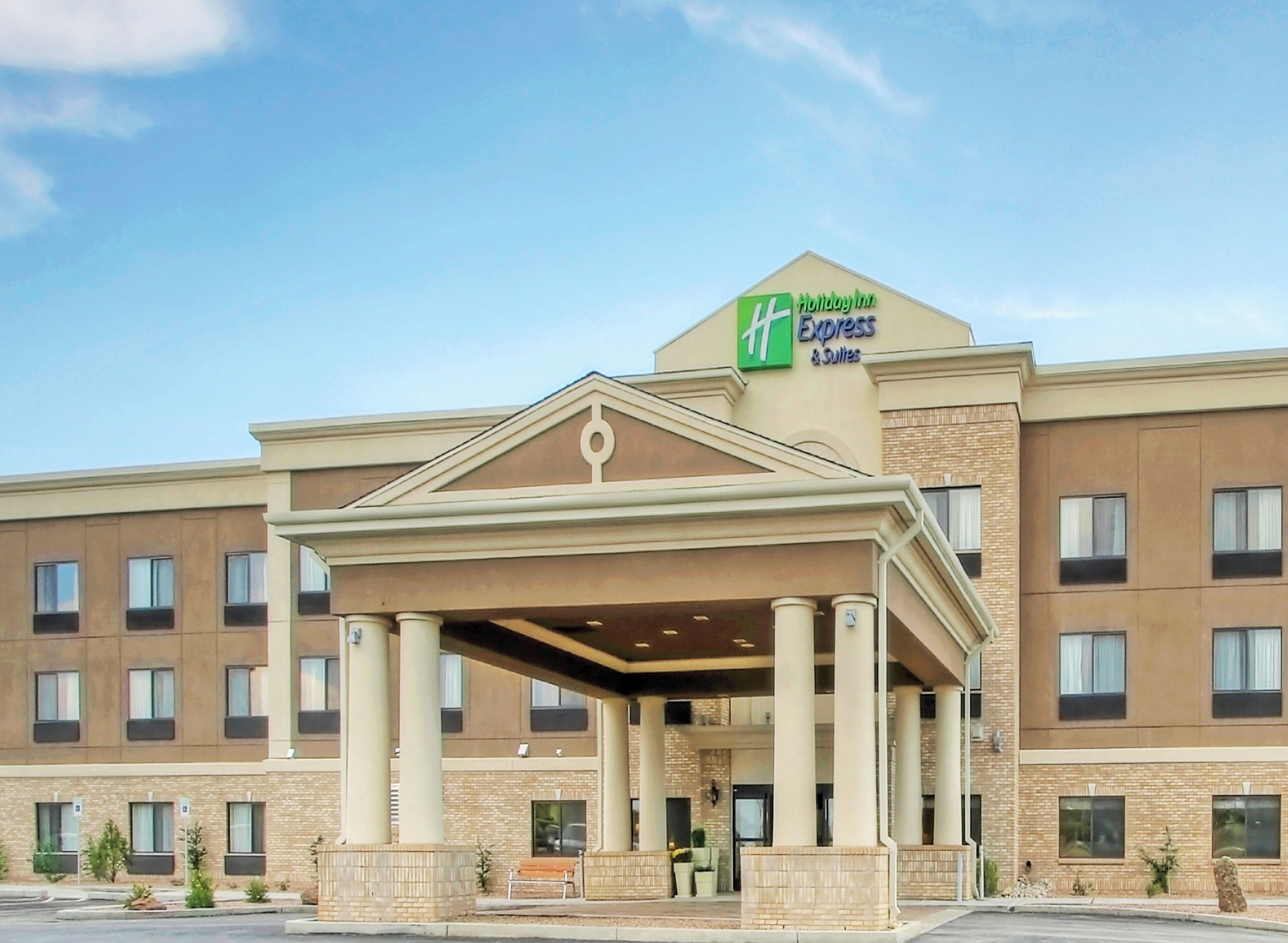 A Holiday Inn Express & Suites building with a covered entrance, multiple windows, and a brick facade.