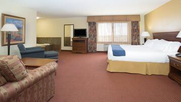 A hotel room with a bed, a sofa, a desk, a television, and a mirror.