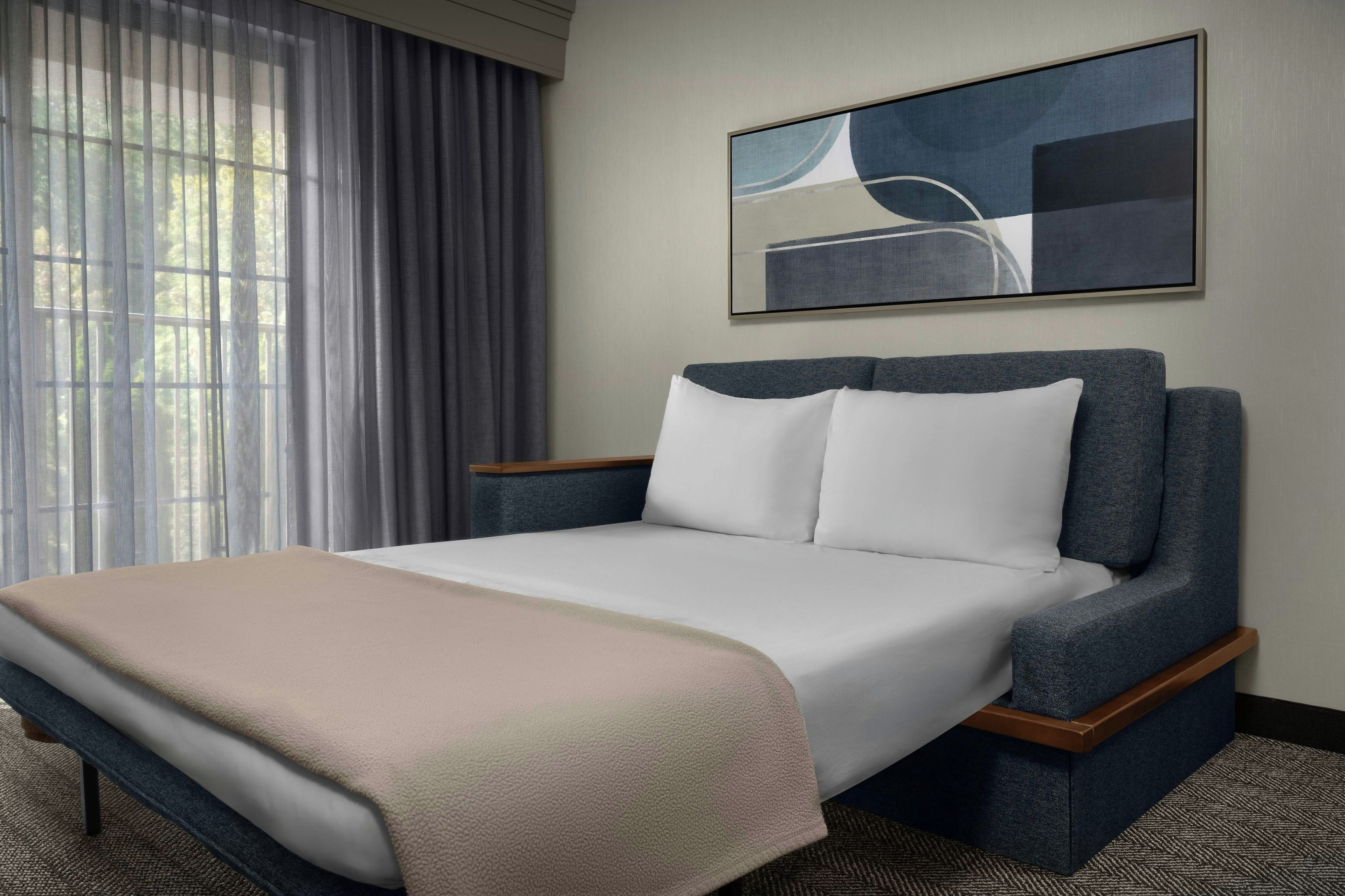 Een hotelkamer met een bed, een raam met gordijnen, een schilderij aan de muur en een vloerbedekking.
