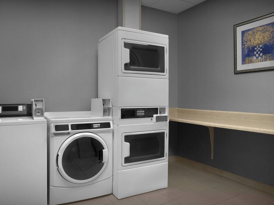 A laundry room with stacked washers and dryers, a control panel, and a wall-mounted artwork.