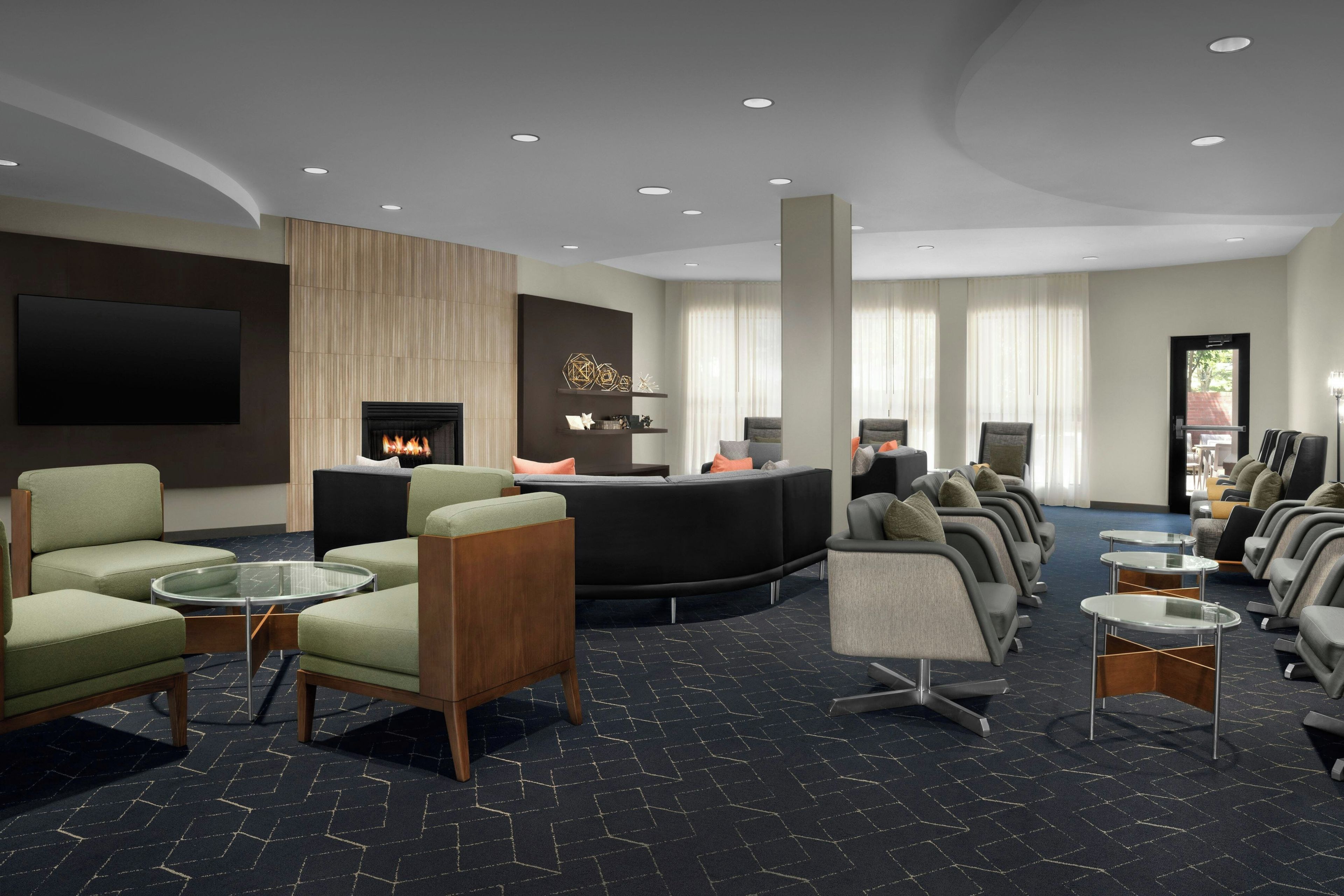 A modern hotel lobby with a fireplace, seating area, and a flat-screen TV mounted on the wall.