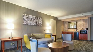 A hotel room with a sofa, armchairs, a coffee table, a desk, a lamp, a kitchen area, and a large mirror. - Courtyard by Marriott Blacksburg (Blacksburg)