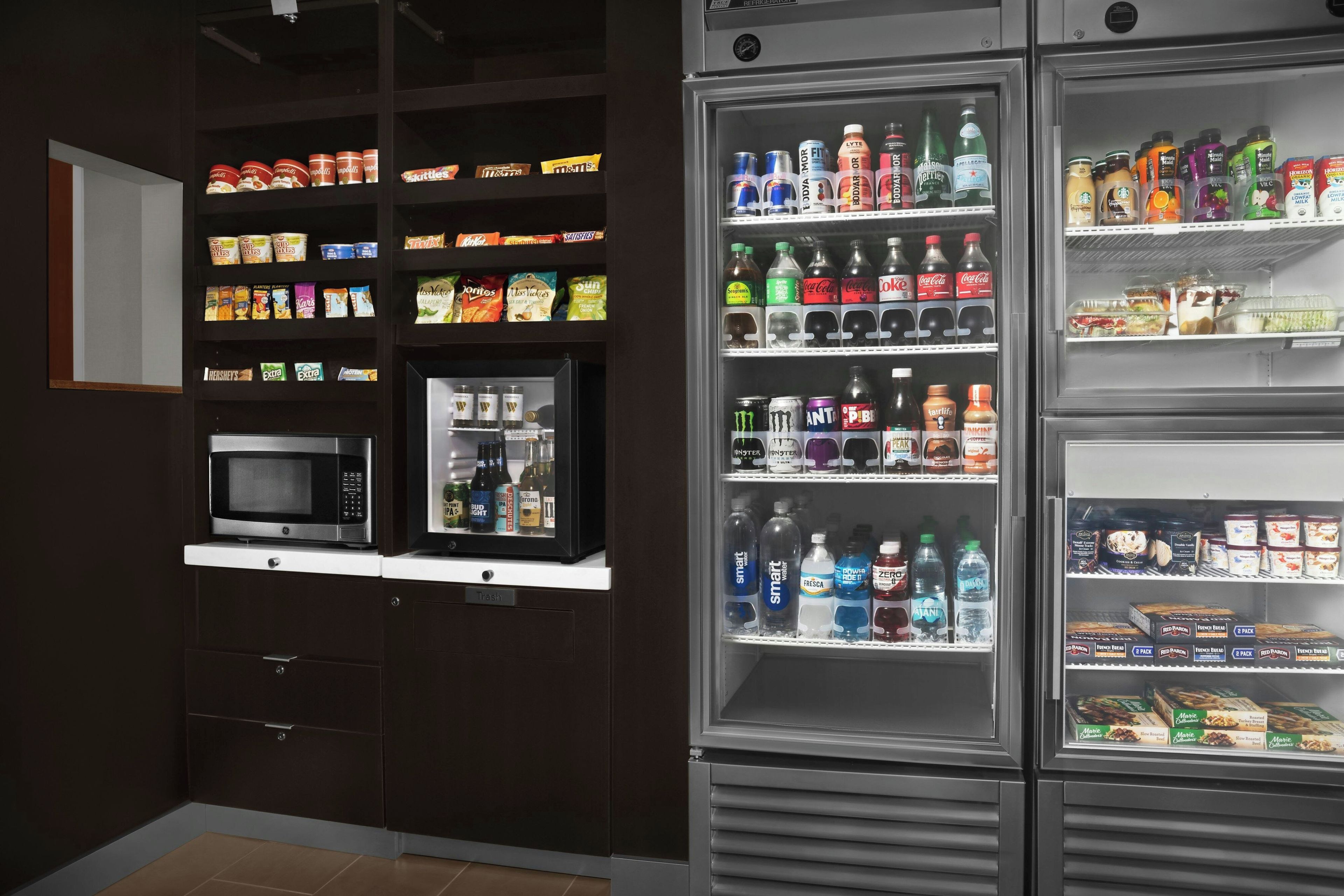 Una kitchenette equipada con microondas, refrigerador y estantes repletos de aperitivos y bebidas.