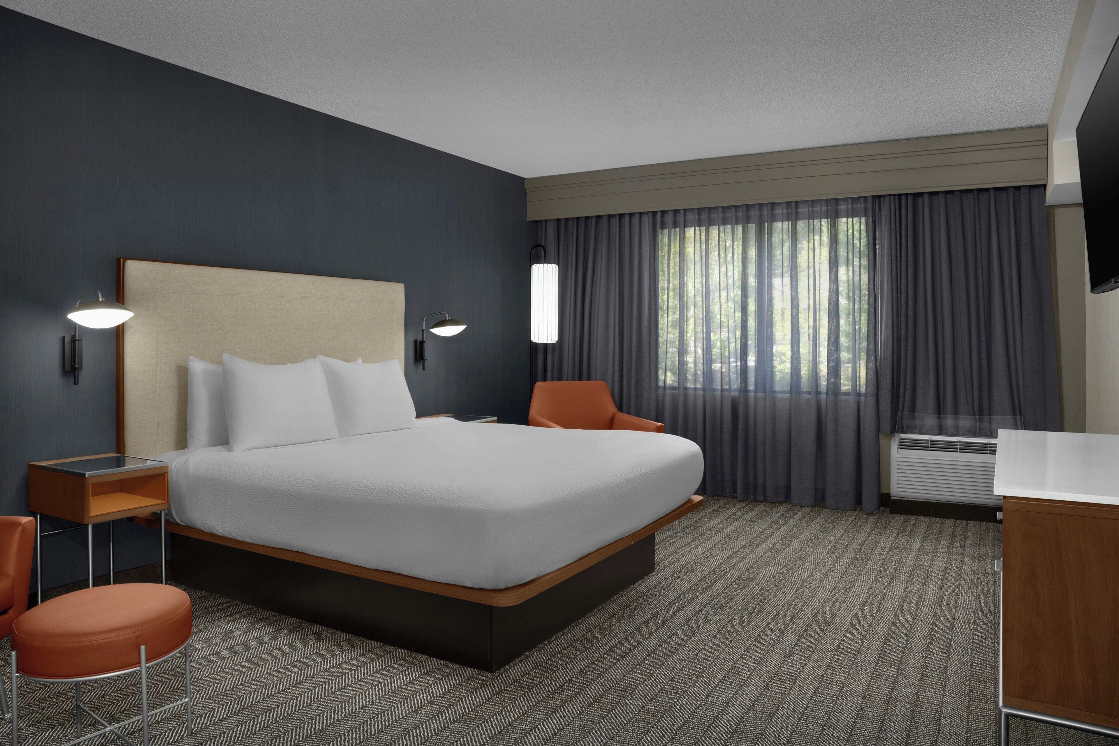A hotel room with a large bed, a desk, a chair, a TV, and a window with curtains.