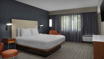 A hotel room with a large bed, a desk, a chair, a TV, and a window with curtains.