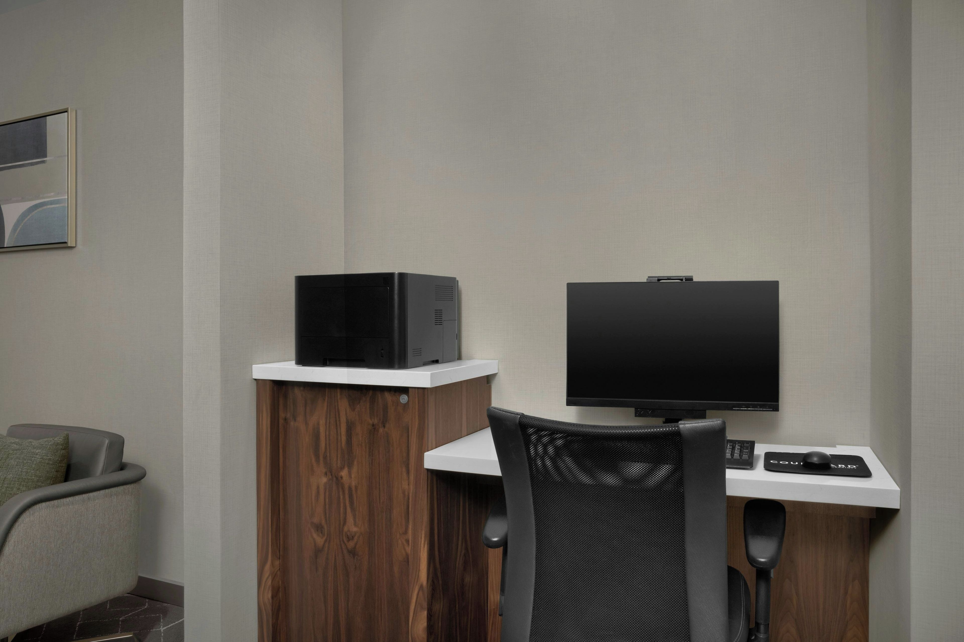 A hotel room with a desk, a computer, a TV, a chair, and a bed.