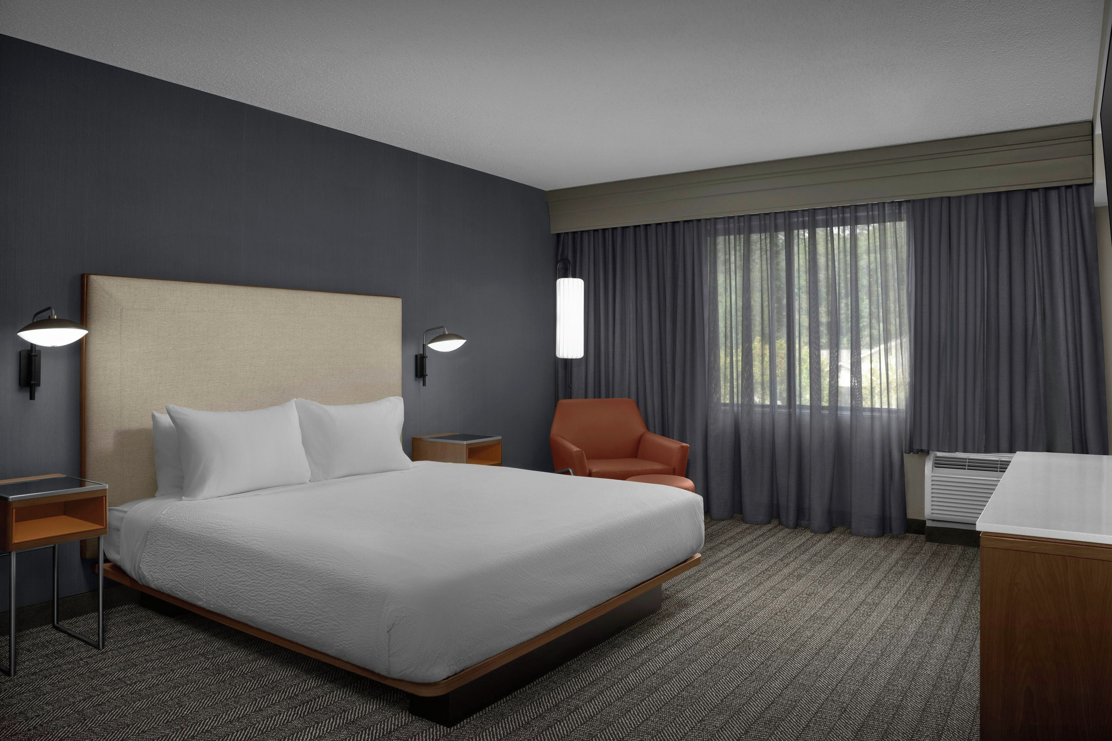 Habitación de hotel con una cama grande, una silla, un escritorio y una ventana con cortinas.