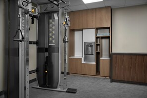 Un gimnasio con una máquina de pesas, armarios de madera y un dispensador de agua.