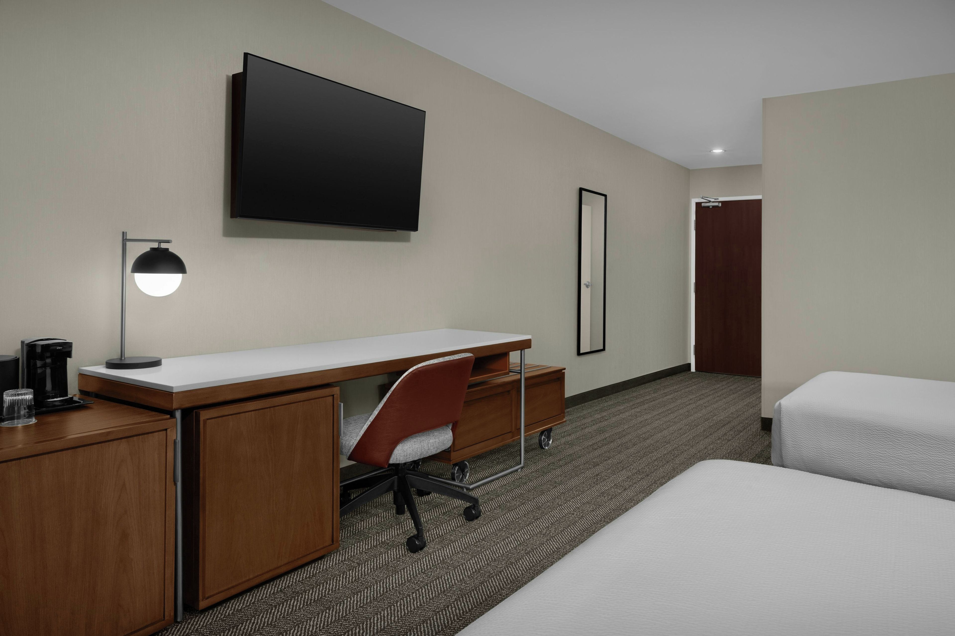 A hotel room with a desk, chair, bed, TV, and a coffee maker.