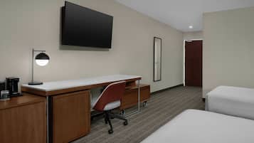 A hotel room with a desk, chair, bed, TV, and a coffee maker.
