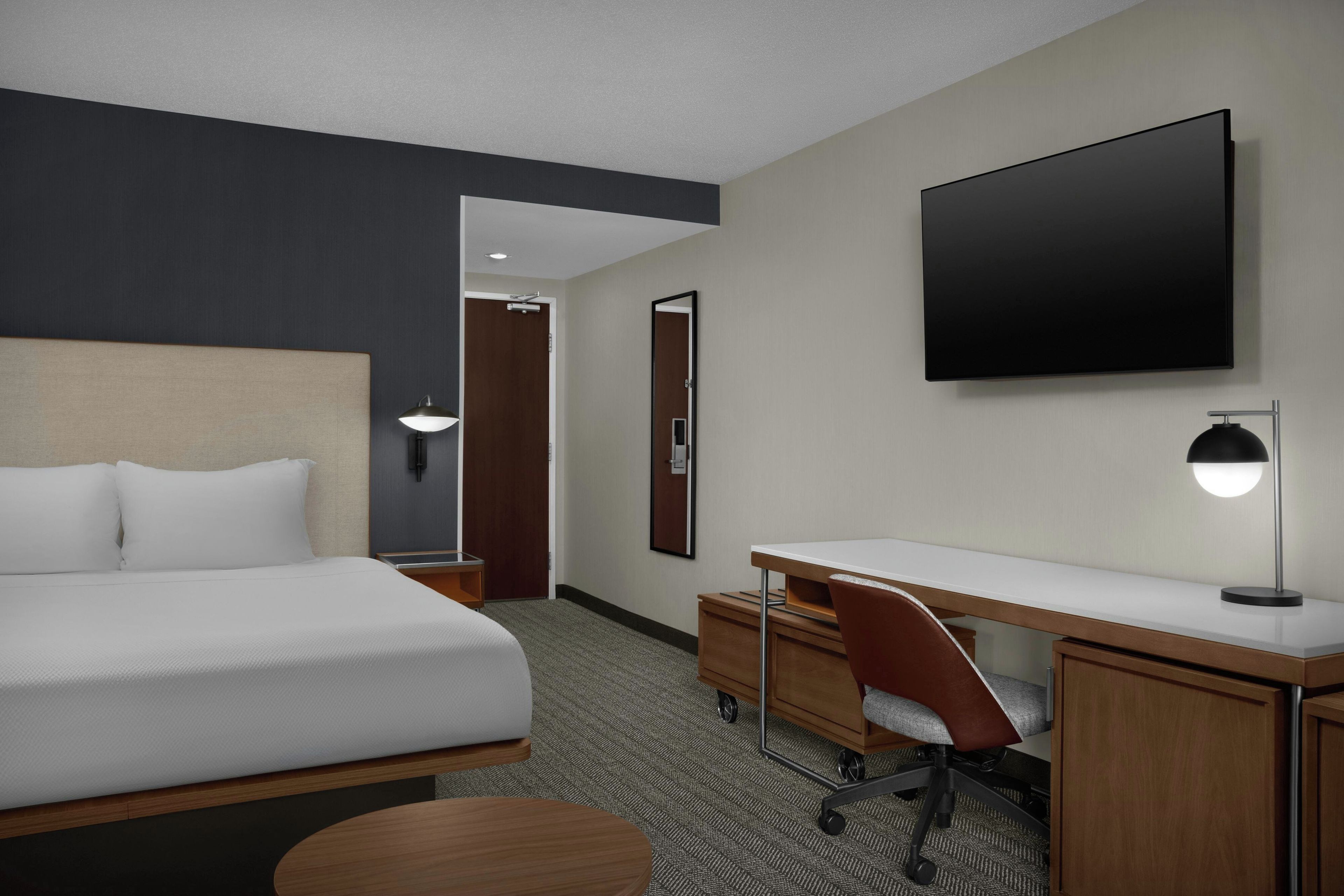 Habitación de hotel con cama, escritorio, silla, televisor y una puerta que da a otra habitación.