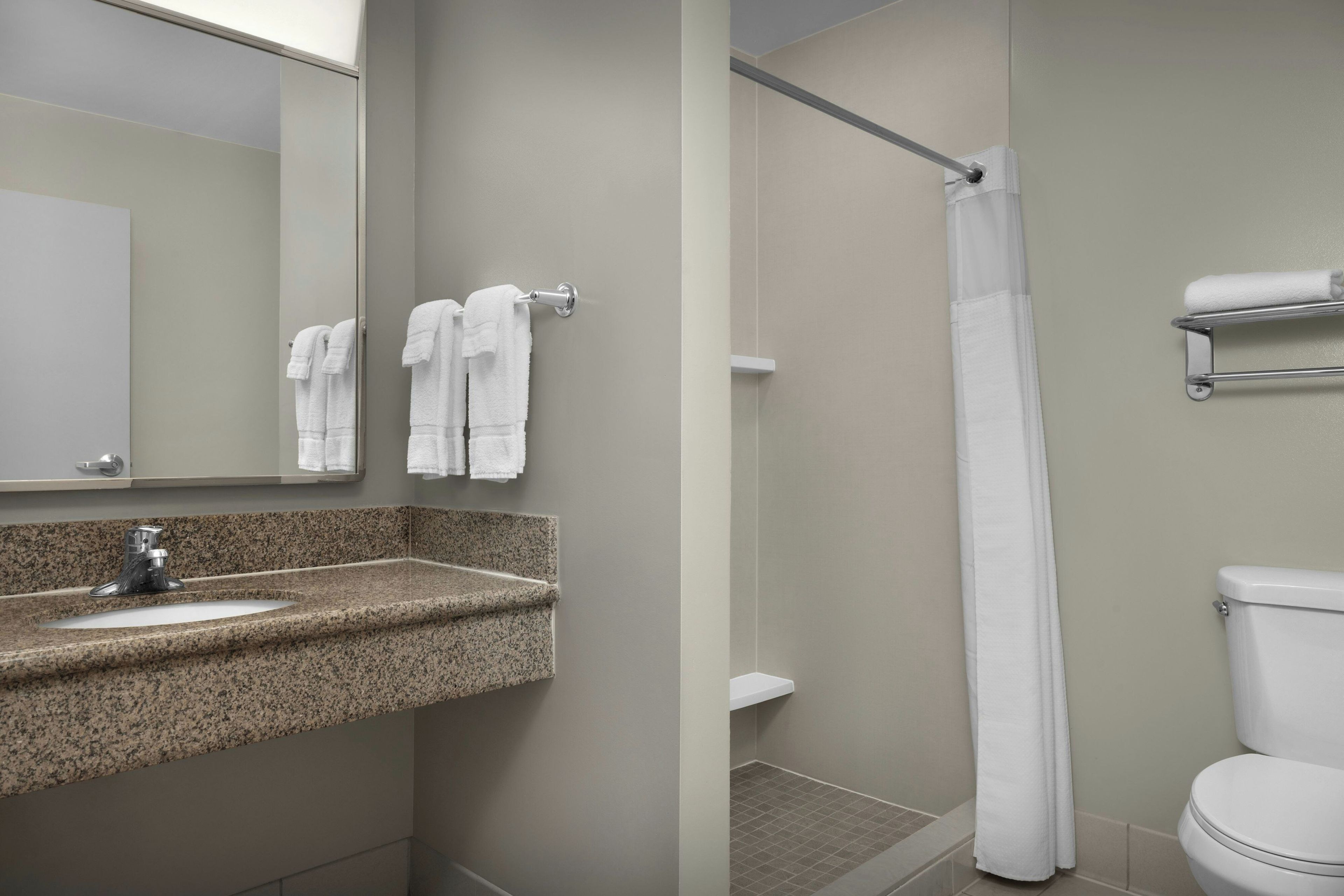 Un baño con lavamanos de encimera de granito, un espejo, un inodoro y una ducha con cortina.