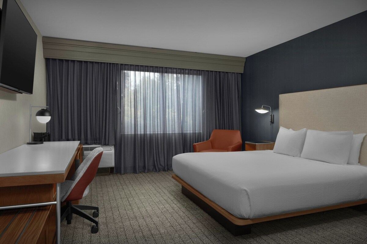 A hotel room with a bed, a desk, a chair, a TV, and a window with curtains.