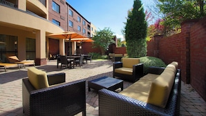 An outdoor patio with wicker furniture, a brick wall, and a clear blue sky. - Courtyard by Marriott Blacksburg (Blacksburg)