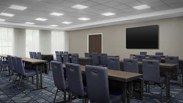Un salón de conferencias con mesas y sillas, una puerta y una pantalla de proyección.