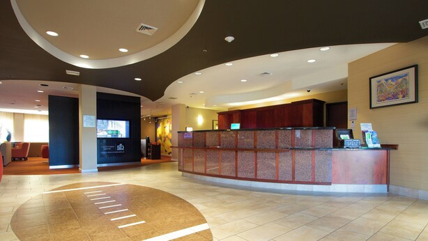 A hotel reception area with a curved reception desk, a large digital screen, and a tiled floor with directional markings. - Courtyard by Marriott Blacksburg (Blacksburg)