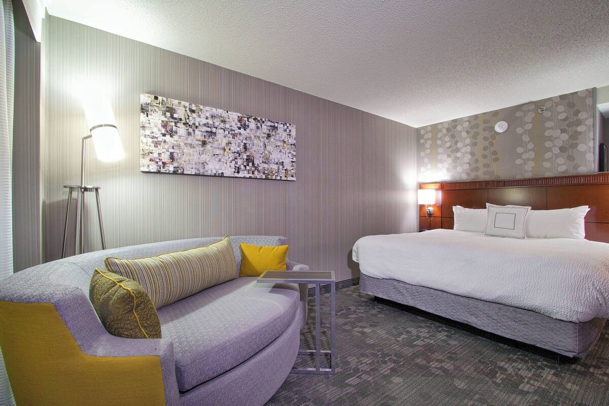 Ein Hotelzimmer mit einem Bett, einem Sofa, einem kleinen Tisch und einem an der Wand hängenden Kunstwerk.