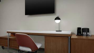 Habitación de hotel con escritorio, silla, televisor de pantalla plana, lámpara de escritorio y cafetera.