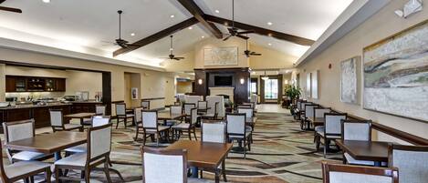 A spacious dining area with multiple tables and chairs, ceiling fans, and a kitchen in the background.