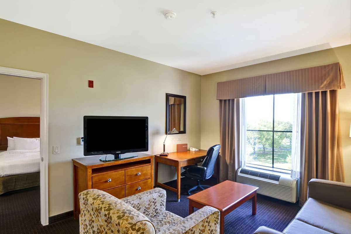 A hotel room with a bed, a desk with a flat-screen TV, a chair, a sofa, and a window with curtains.