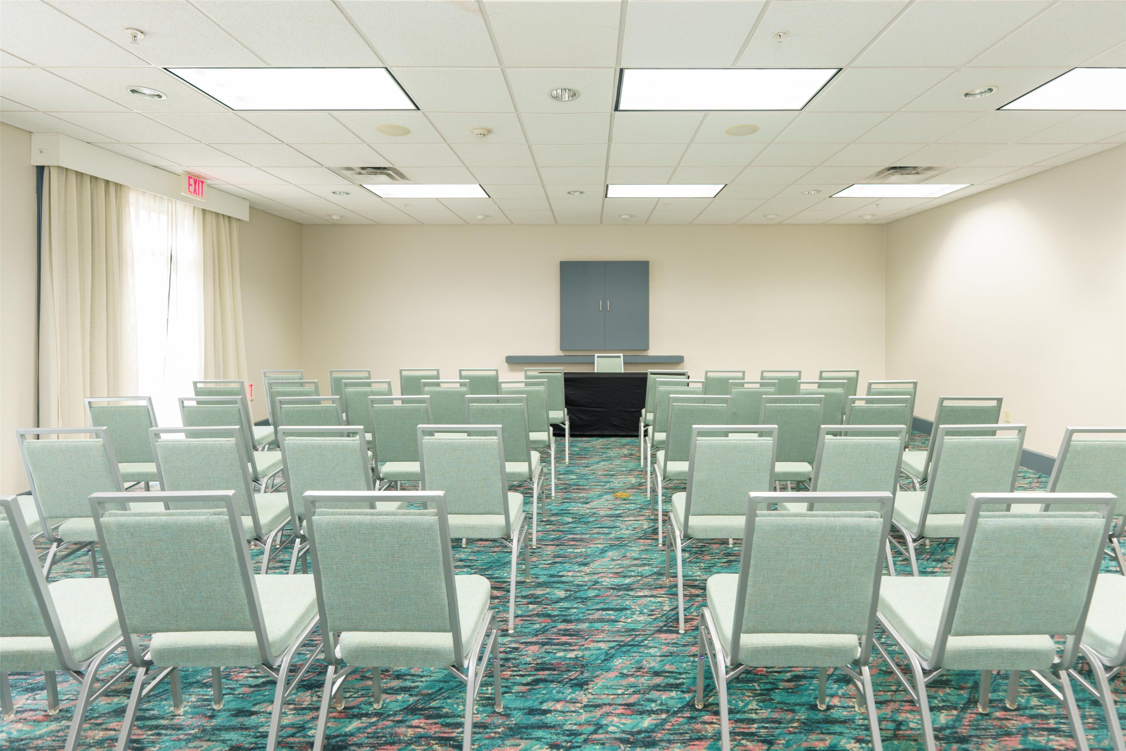 A conference room with rows of chairs, a carpeted floor, and a door marked "EXIT".