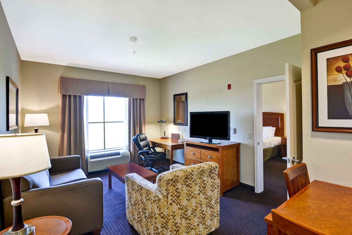 A hotel room with a sofa, armchair, desk, flat-screen TV, and a bed.