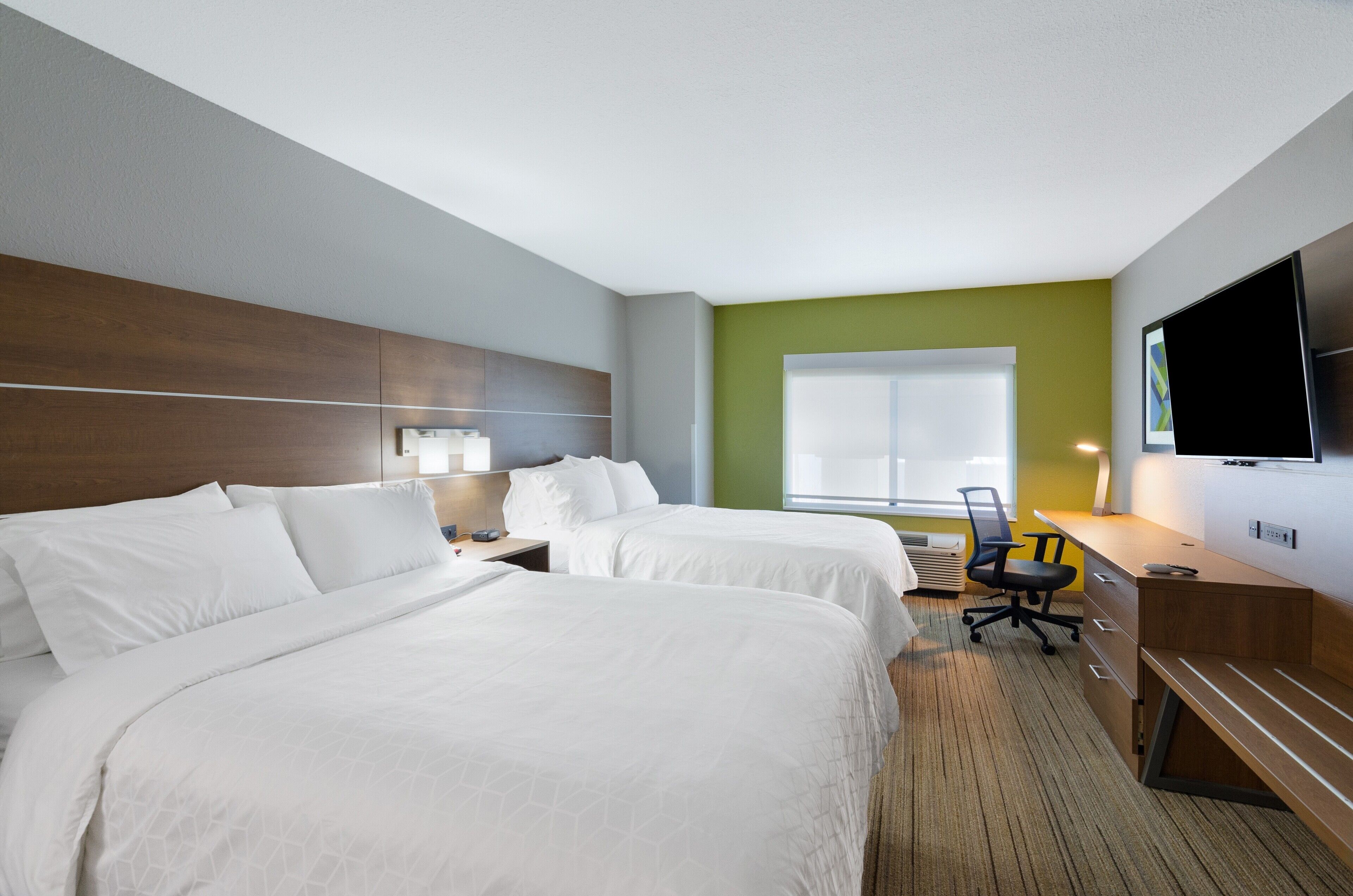 A hotel room with two beds, a desk, a chair, a TV, and a window.