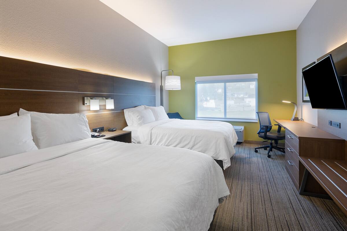A hotel room with two beds, a desk, a chair, a TV, and a window.