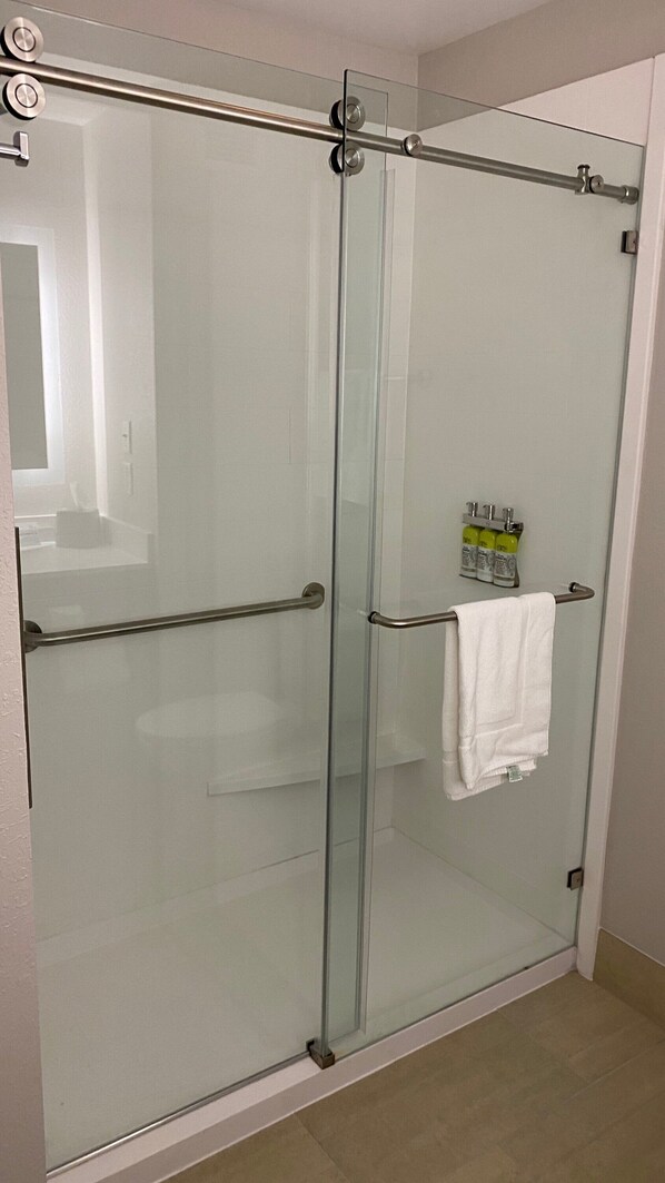 A glass-enclosed shower with a towel rack and a bottle of shampoo.