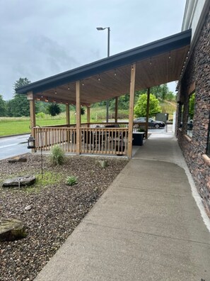 A covered outdoor area with a wooden deck and stone wall, leading to a building entrance.
