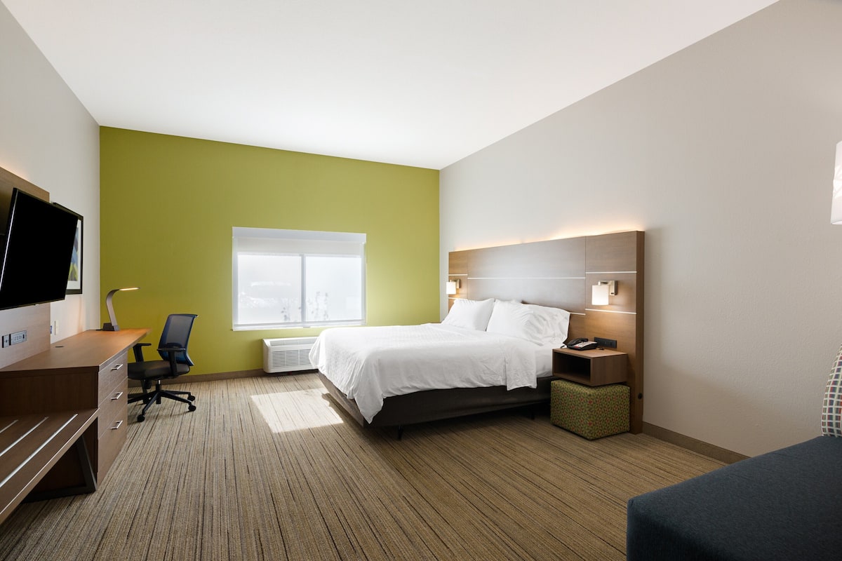 A hotel room with a bed, a desk, a chair, a TV, and a window.