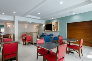 A modern dining area with red and blue chairs, wooden tables, and a flat-screen TV mounted on the wall. - Holiday Inn Express Hotel & Suites Weston by IHG (Weston)