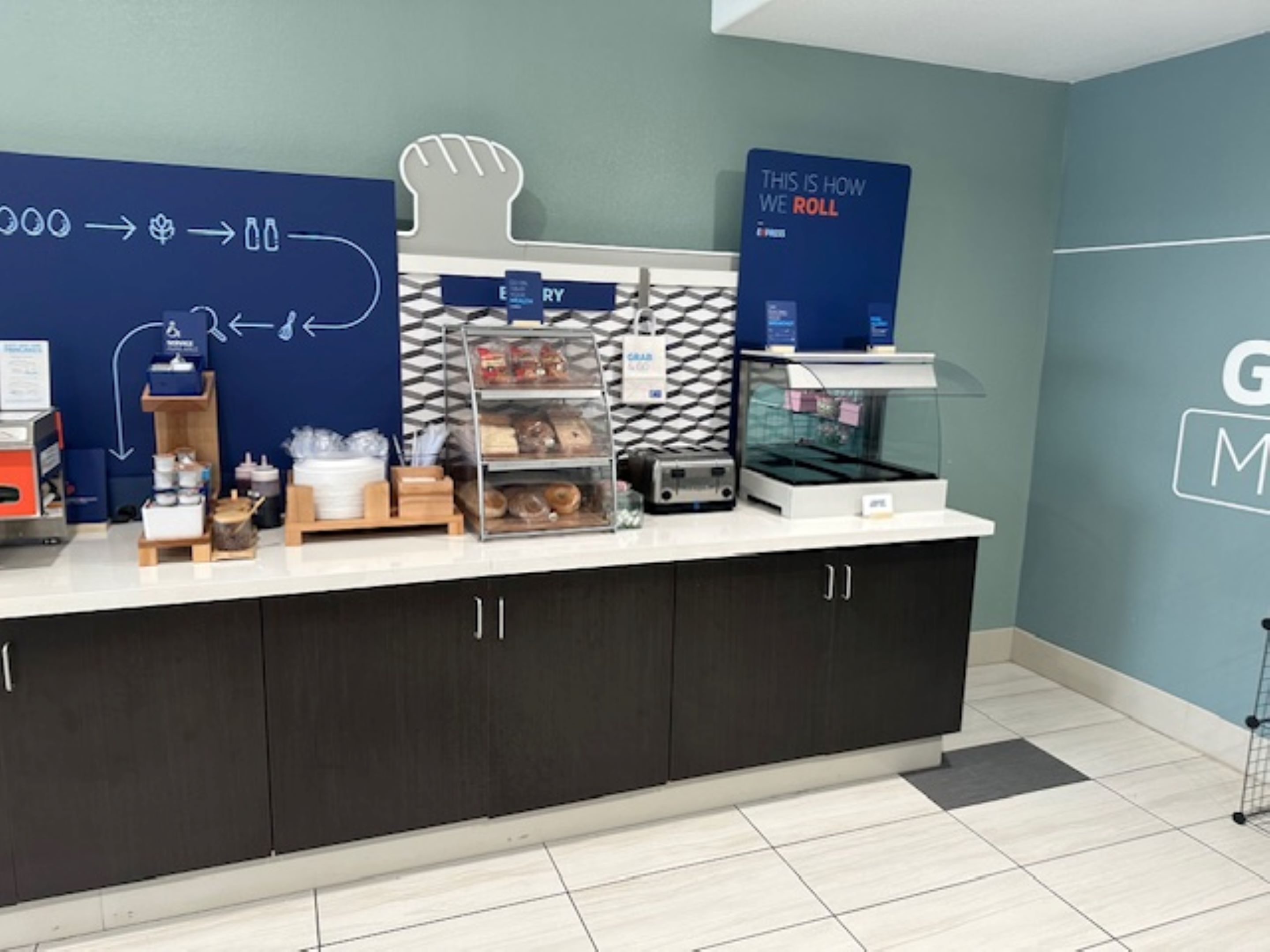 A breakfast station with a variety of food items, a chalkboard with writing, and a sign that says "THIS IS HOW WE ROLL".