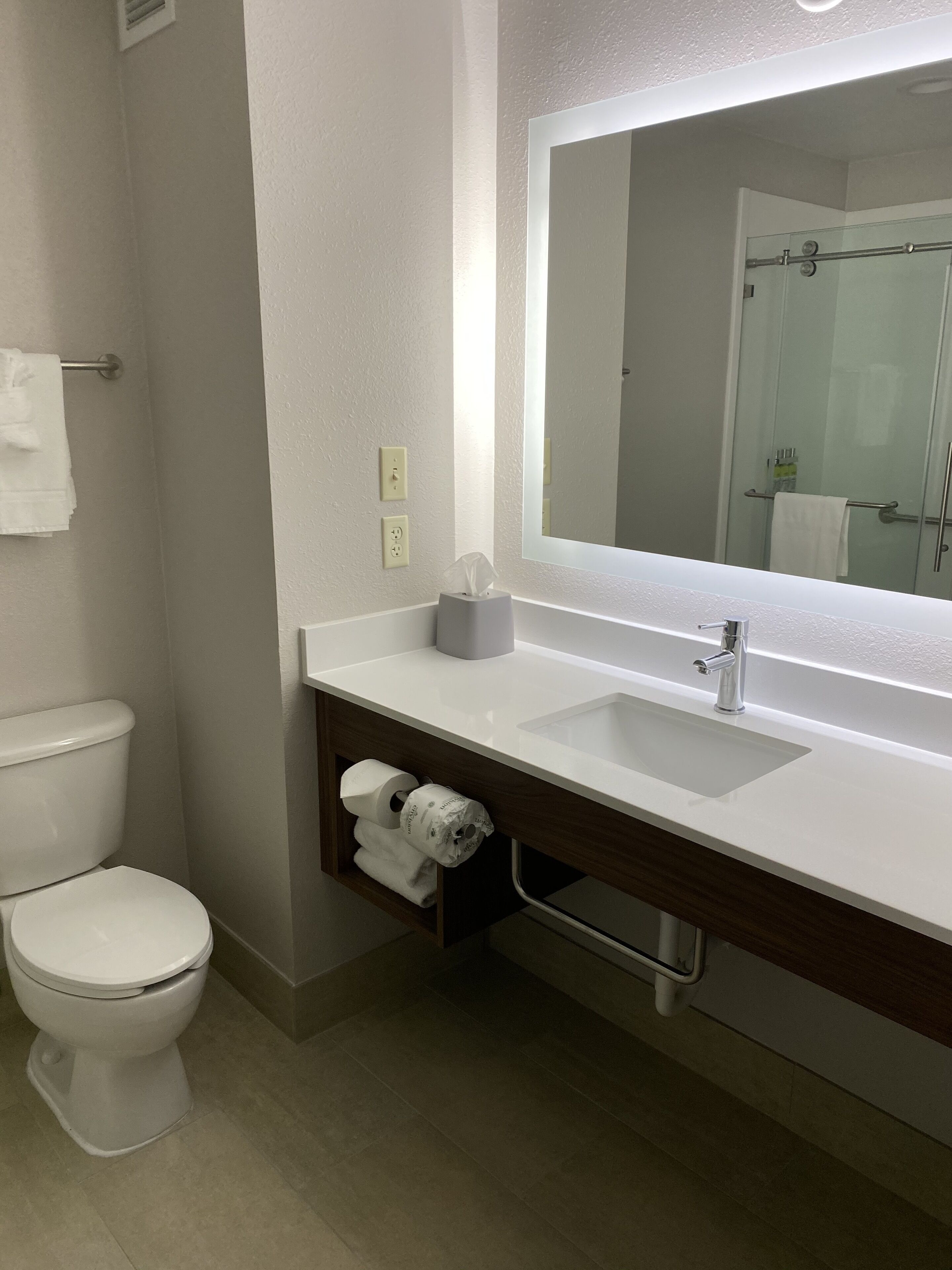 Une salle de bain moderne avec des toilettes blanches, un lavabo surmonté d’un miroir et un porte-serviettes.