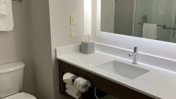 Une salle de bain moderne avec des toilettes blanches, un lavabo surmonté d’un miroir et un porte-serviettes.