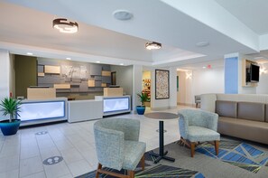 A hotel lobby with a reception desk, seating area, and a small kitchenette. - Holiday Inn Express Hotel & Suites Weston by IHG (Weston)
