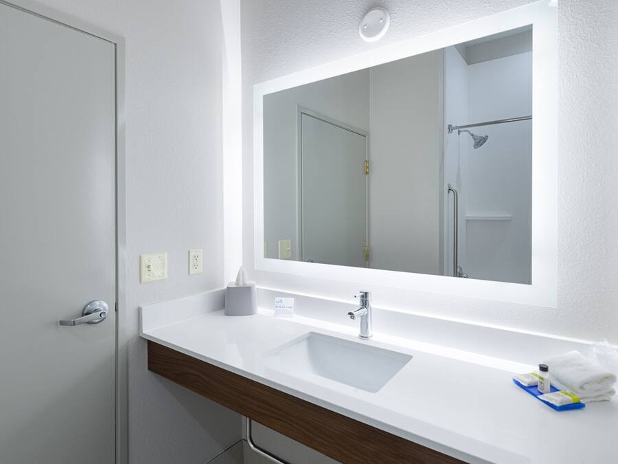 Un baño moderno con un lavamanos blanco, un espejo grande y una zona de ducha.