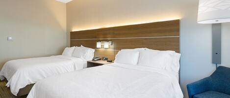 A hotel room with two beds, a desk, a chair, and a lamp.