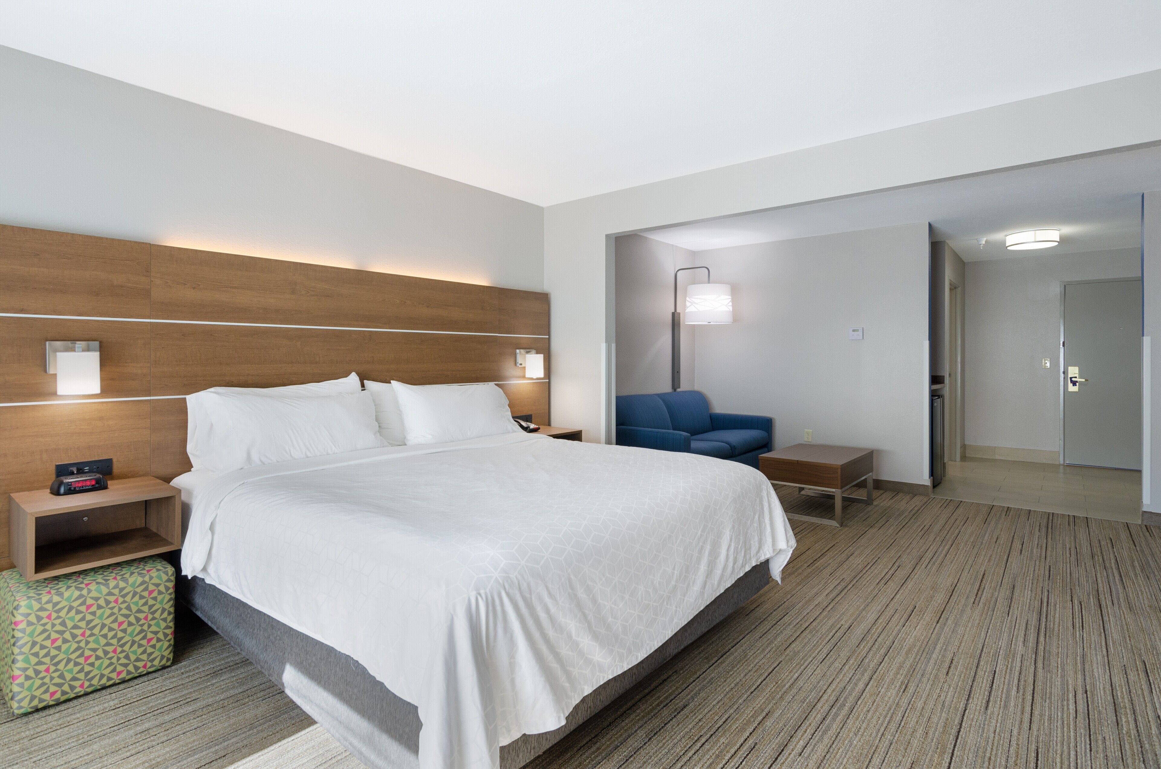Een moderne hotelkamer met een groot bed, nachtkastjes, een bureau, een stoel en een spiegel.