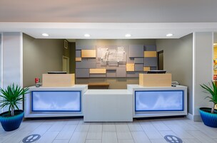 Un área de recepción de hotel moderna, con un mostrador central, dos mostradores laterales y un letrero en la pared.