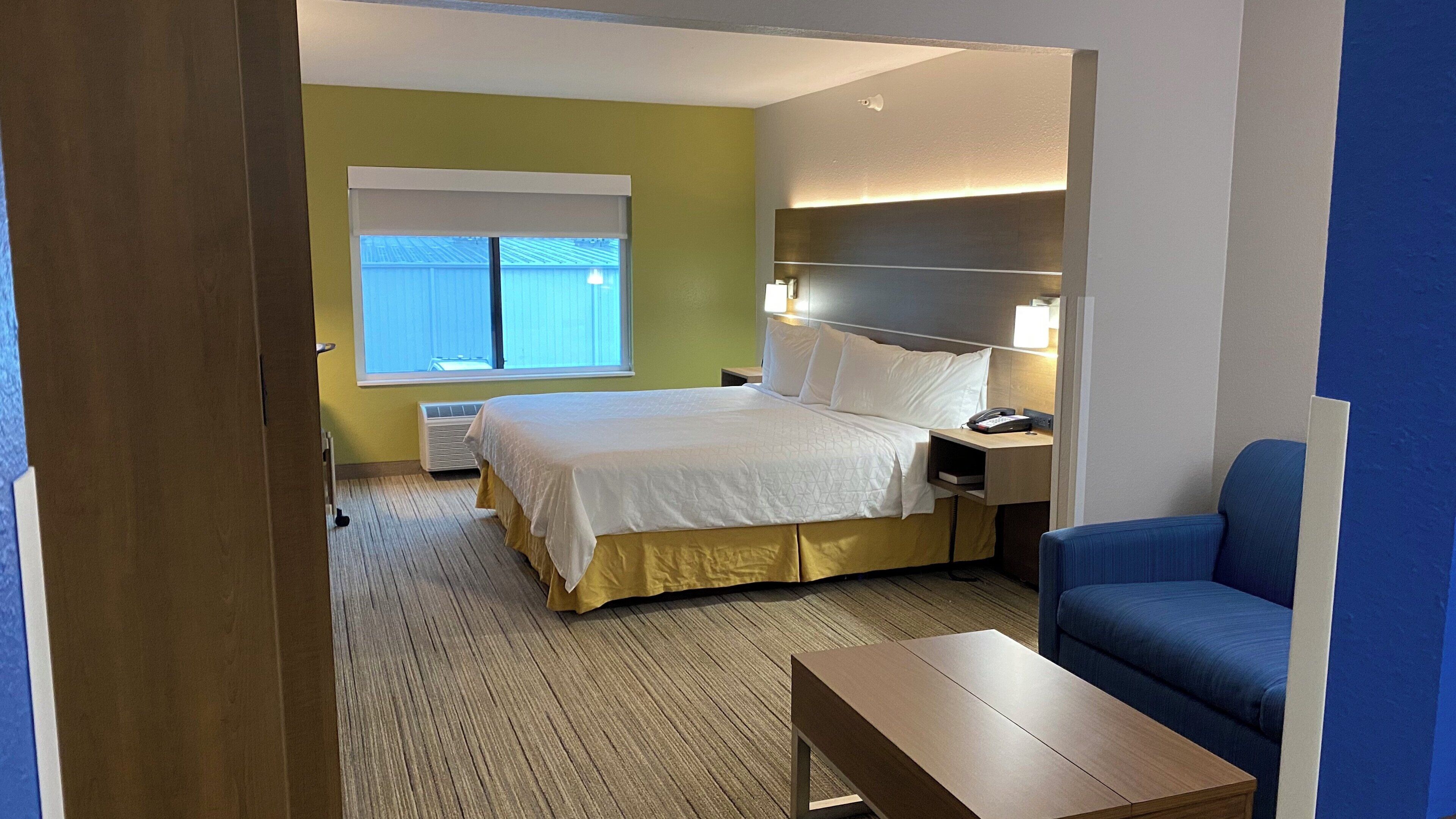 A hotel room with a bed, bedside table, lamp, and a blue chair.