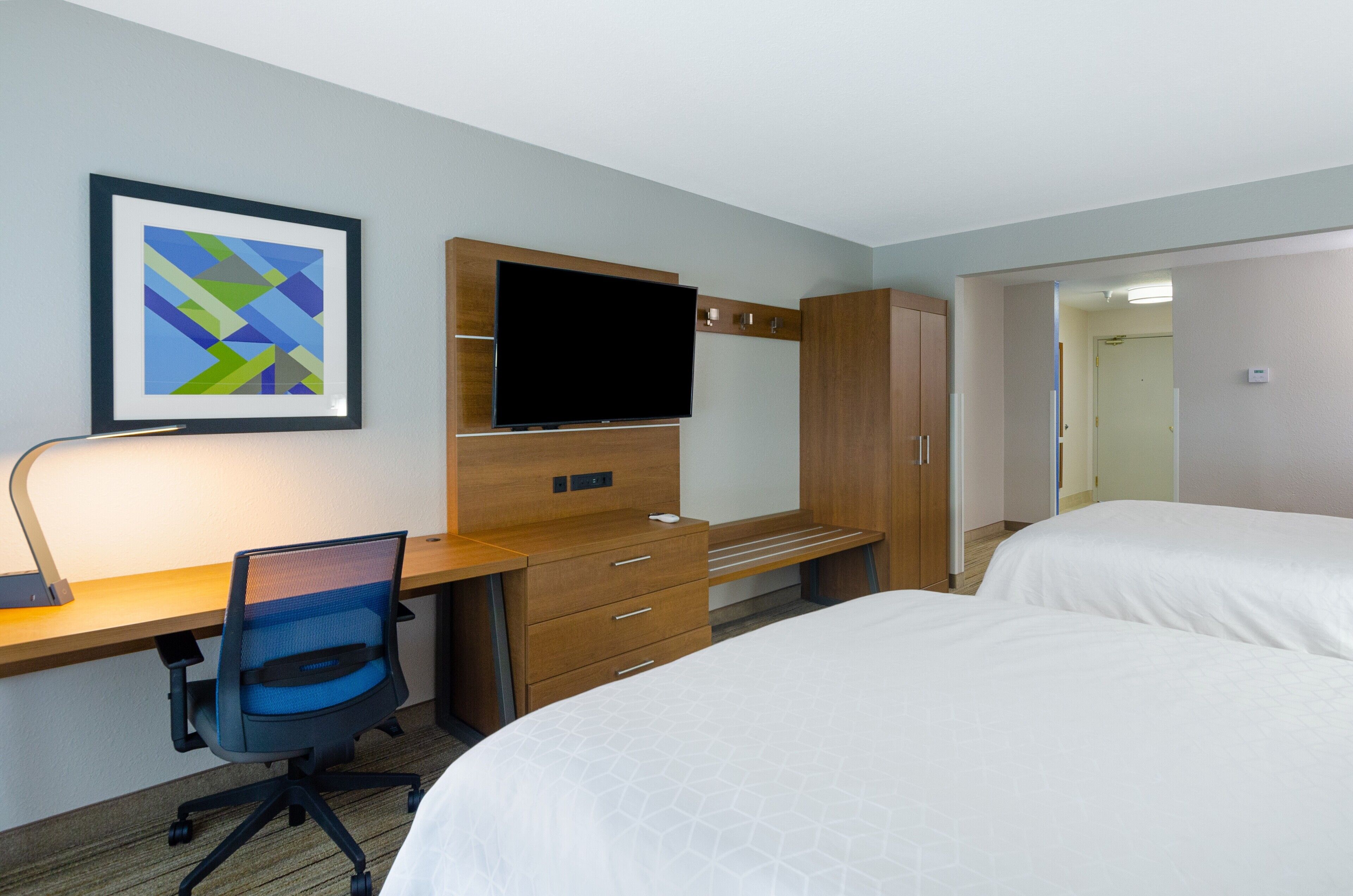 Ein Hotelzimmer mit Schreibtisch, Fernseher, Bett und einer Tür zu einem anderen Raum.