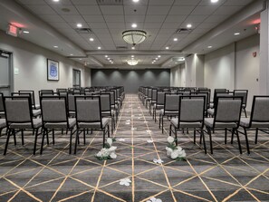 Une salle de conférence avec des rangées de chaises, une moquette à motifs et un lustre.